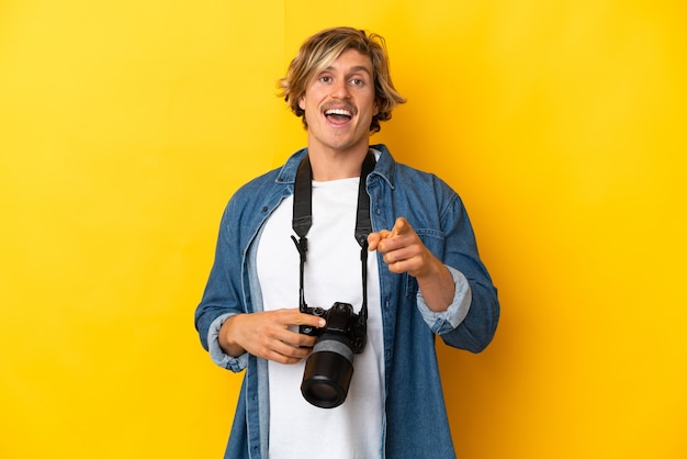 Photo young photographer man isolated on yellow background surprised and pointing front