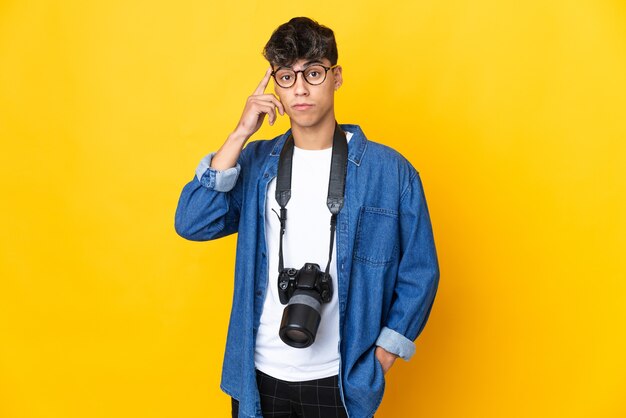 Young photographer man over isolated yellow background thinking an idea