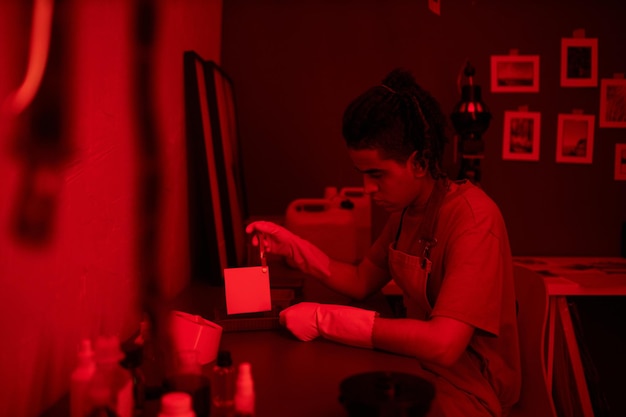 Young photographer putting photos in water in darkroom