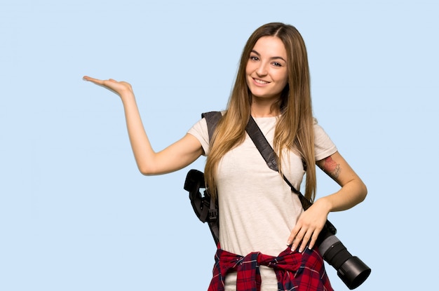 Young photographer woman holding copyspace imaginary on the palm to insert an ad on isolated blue background