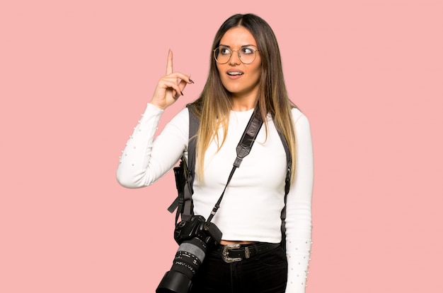 Young photographer woman intending to realizes the solution while lifting a finger up on isolated pink background