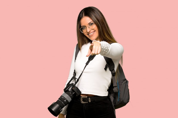 Young photographer woman points finger at you with a confident expression on isolated pink wall