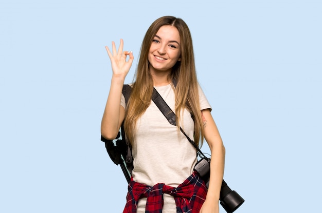 Young photographer woman showing an ok sign with fingers on isolated blue background