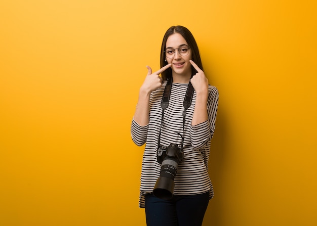 Young photographer woman smiles, pointing mouth