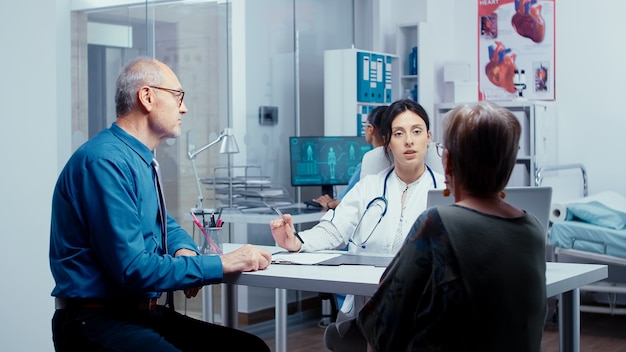 Giovane medico che consulta una vecchia coppia di pensionati riguardo al loro problema. controllo sanitario moderno dell'ospedale o della clinica privata per la prevenzione delle malattie e problemi sanitari. reclami dei pazienti e medicare