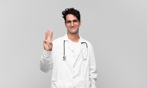 Young physician smiling and looking friendly, showing number two or second with hand forward, counting down