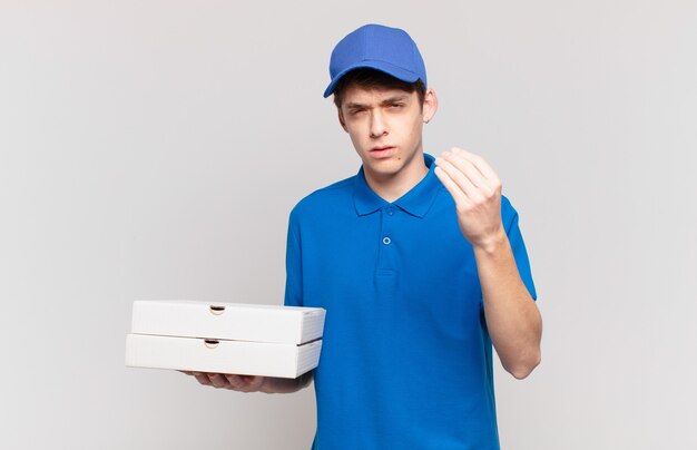 Young pizza deliver boy making capice or money gesture, telling you to pay your debts!