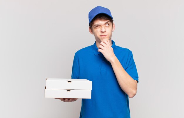 Young pizza deliver boy thinking, feeling doubtful and confused, with different options, wondering which decision to make