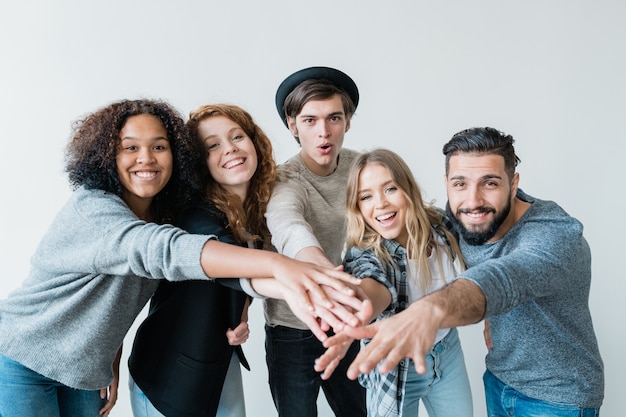 Young playful intercultural friends in casualwear looking at you with smiles while stretching arms forwards