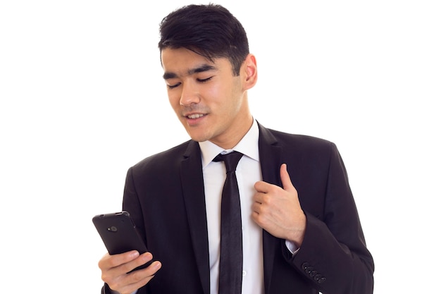 Young pleasant man with black hair in white shirt and black suit with tie using his phone