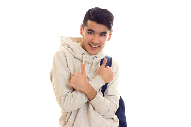 Young pleasant man with dark hair in white hoody with blue backpack on white background in studio