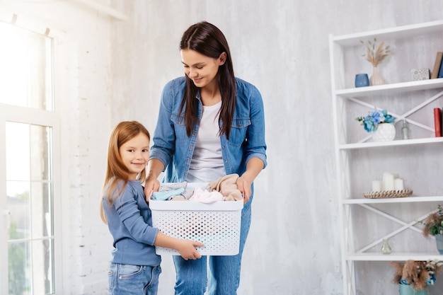 Foto giovane famiglia contenta che tiene insieme il contenitore con i vestiti mentre si prepara per l'attività di lavaggio