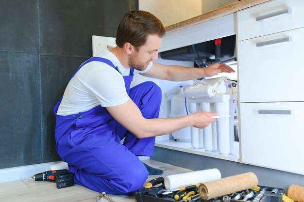 Photo young plumber or technician installing or repairing system of water filtration