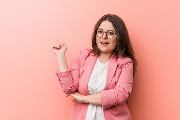 Young plus size business caucasian woman smiling cheerfully pointing with forefinger away.