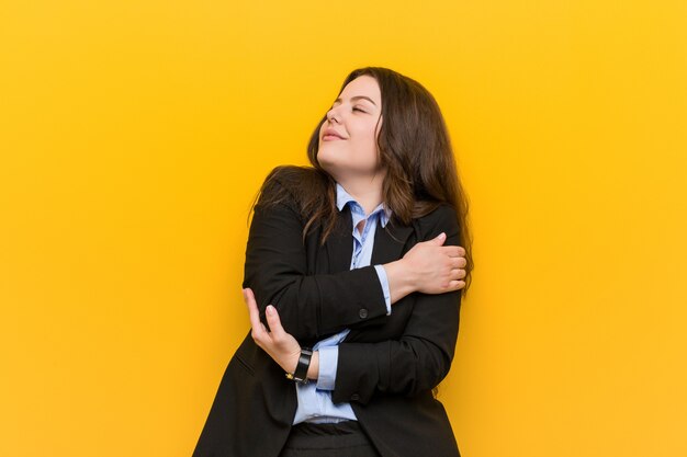 Young plus size caucasian business woman hugs himself, smiling carefree and happy.