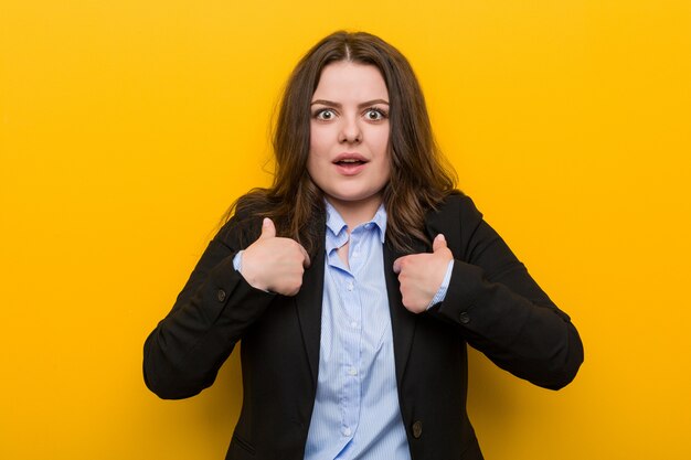 Young plus size caucasian business woman surprised pointing at himself, smiling broadly.