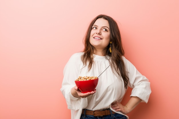 Young plus size curvy woman holding a cereals bowl smiling confident with crossed arms.