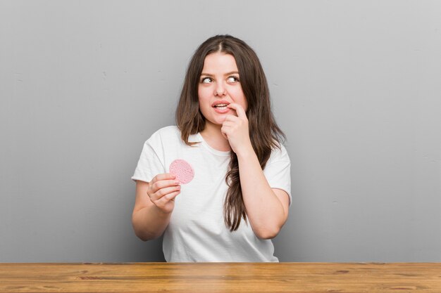 Young plus size curvy woman holding a facial sponge relaxed thinking about something looking at a copy space.