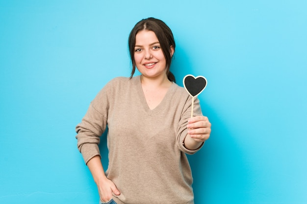 Young plus size curvy woman holding a heart shape happy, smiling and cheerful.