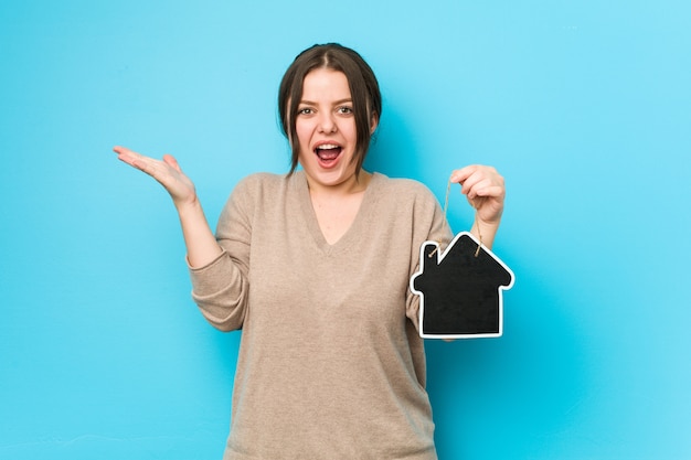 Photo young plus size curvy woman holding a home icon celebrating a victory or success