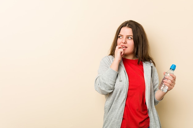 Young plus size curvy woman holding a water bottle relaxed thinking about something