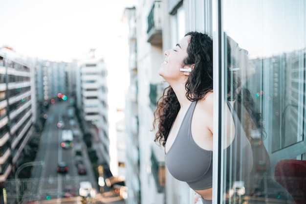 Young plus size woman in sportswear influencer inspiring air outside balcony listening music and relaxing after a day of training. Mental health and happy new habits concept