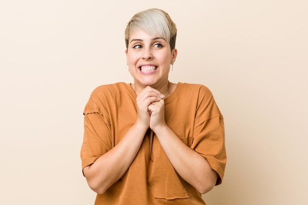 Young plus size woman with short hair keeps hands under chin, is looking happily aside.