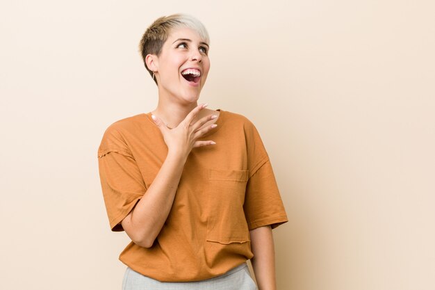 Young plus size woman with short hair laughs out loudly keeping hand on chest.