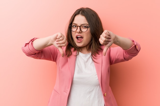 Young plus size zakelijke blanke vrouw duim omlaag tonen en afkeer uiten.