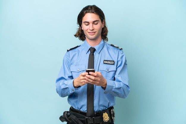 Young police caucasian man isolated on blue background sending\
a message with the mobile