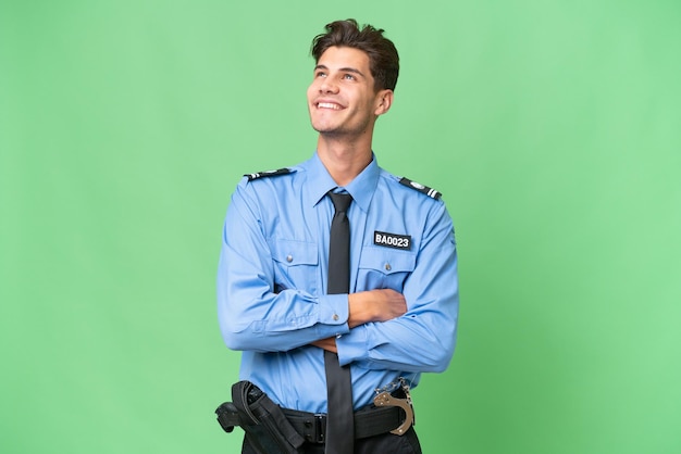Молодой полицейский на изолированном фоне смотрит вверх, улыбаясь