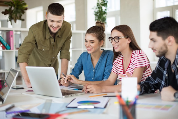 Young positive business people joyfully working on laptop together Group of smiling men and women spending time at work in modern cozy office