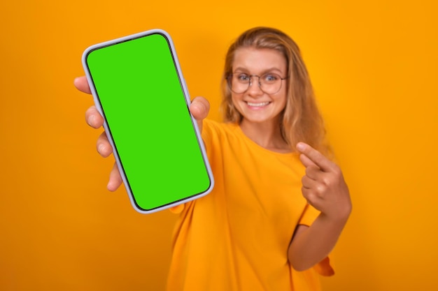 젊은 긍정적 인 백인 여성이 녹색 화면으로 모의 휴대전화를 들고 있습니다.