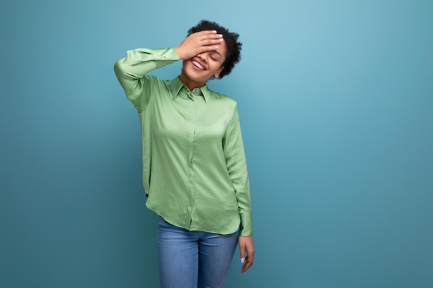 Foto giovane modella femminile positiva con i capelli neri ricci vestita con una camicia verde e jeans sta sorridendo