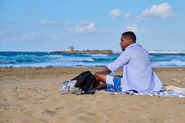 해변에 앉아 쉬고 있는 젊은 긍정적인 남성 관광객