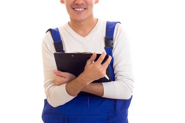 Young positive man in white shirt and blue overall holding white pen and black folder