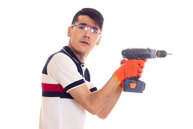 Young positive man with orange gloves and protective glasses holding grey electric screwdriver