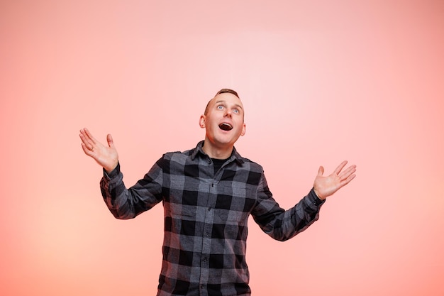 Young positive smiling man in a checkered shirt on a pink background Place for text