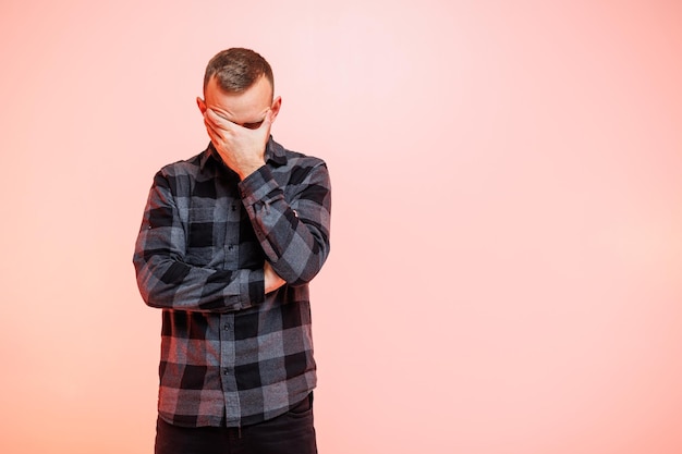 Young positive smiling man in a checkered shirt on a pink background Place for text