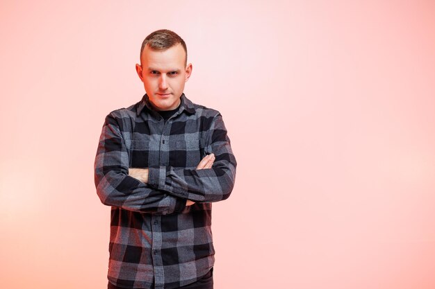 Young positive smiling man in a checkered shirt on a pink background Place for text