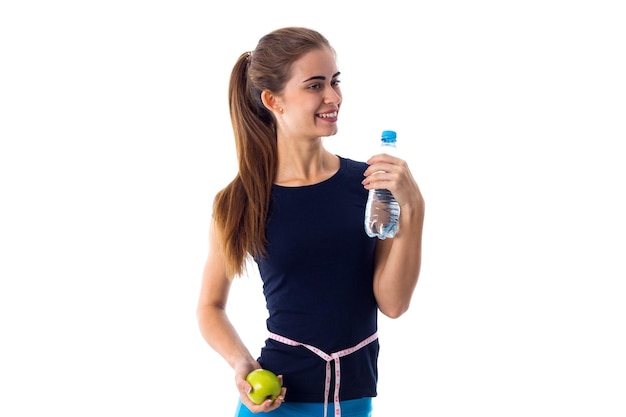 Young positive woman in blue Tshirt with centimeter around her neck holding green apple in studio