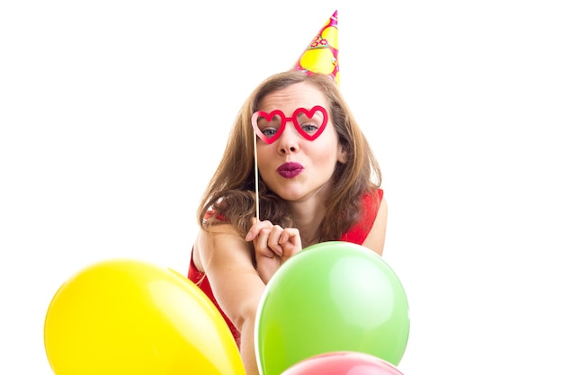 Young positive woman celebrating hat holding many colored balloons and card stick of glasses