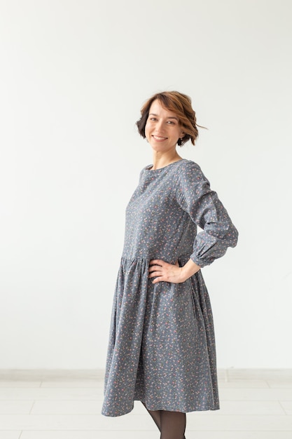 Young positive woman in gray dress posing against white wall. Concept elegant casual dress.