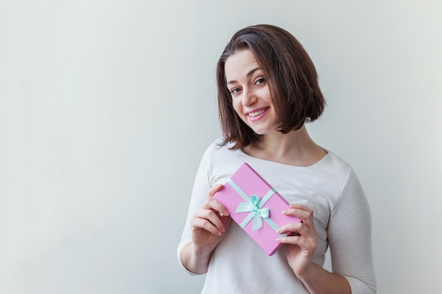 Giovane donna positiva che tiene una piccola scatola regalo rosa isolata su sfondo bianco preparazione per le vacanze...