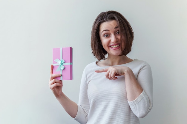 Giovane donna positiva che tiene una piccola scatola regalo rosa isolata su sfondo bianco preparazione per le vacanze...