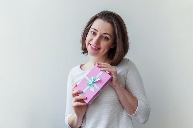 흰색 배경에 격리된 작은 분홍색 선물 상자를 들고 있는 긍정적인 젊은 여성