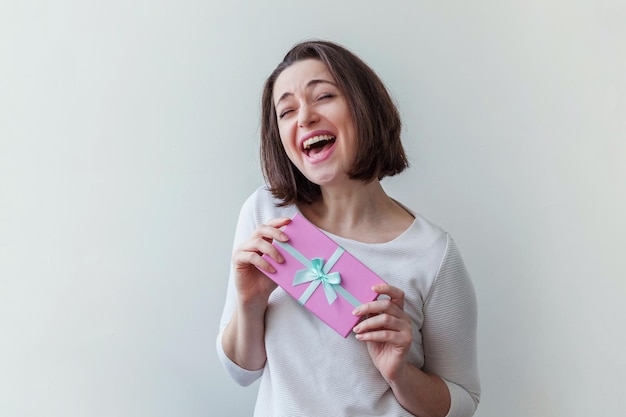 Young positive woman holding small pink gift box isolated on white background preparation for holida...