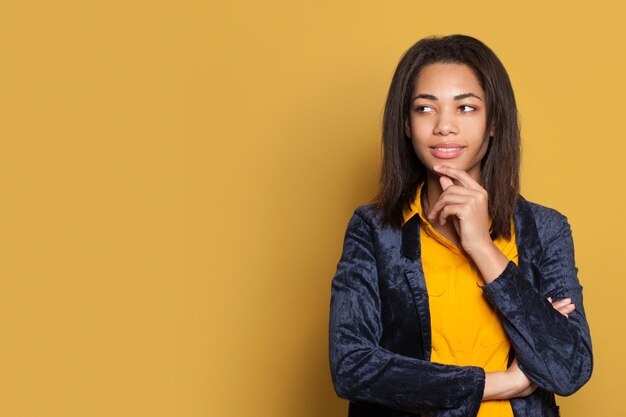 Young positive woman smiling and looking away on yellow background