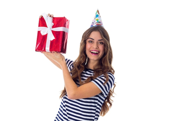 Young positive woman in stripped Tshirt and celebration cap holding red present and looking at it