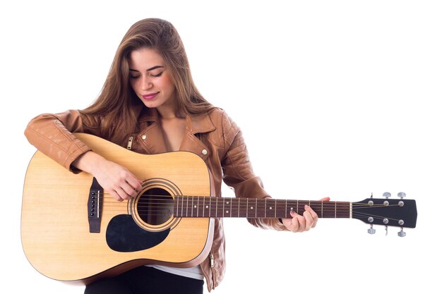 Young positive woman with long hair in brown jacket and black trousers holding a guitar in studio